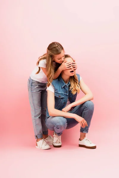 Child in jeans covering eyes of mother wearing denim clothes on pink — Stock Photo