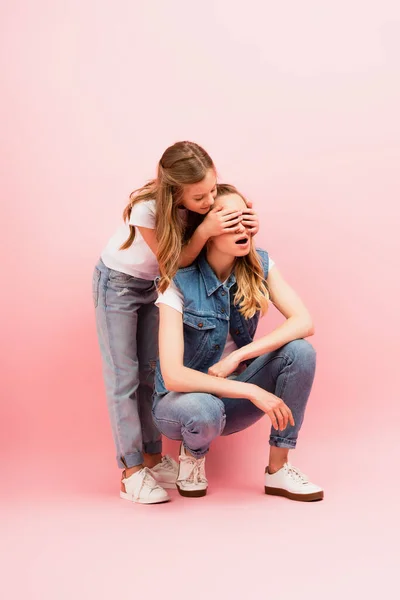 Enfant en jeans couvrant les yeux de la mère portant des vêtements en denim sur rose — Photo de stock