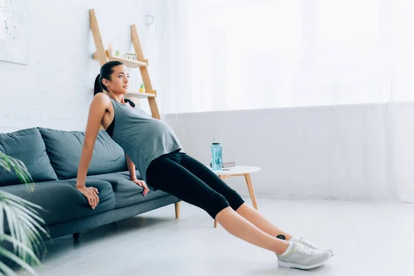 Focus selettivo della sportiva incinta che esercita vicino al divano in soggiorno — Foto stock