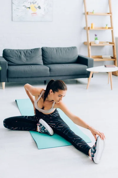 Junge Frau in Sportkleidung wärmt sich zu Hause auf Fitnessmatte auf — Stockfoto