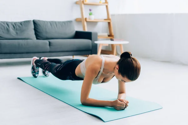 Focus selettivo della sportiva che fa tavola sul tappeto fitness a casa — Foto stock