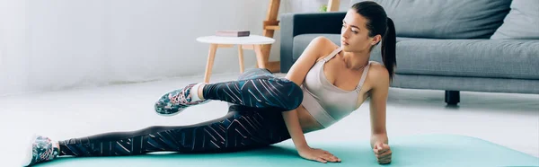 Horizontal image of sportswoman training leg on fitness mat at home — Stock Photo