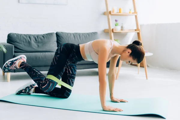 Sportiva bruna che si allena con fascia di resistenza sul tappeto fitness a casa — Foto stock