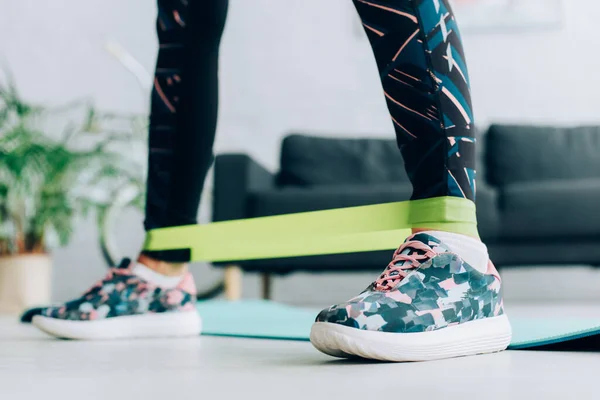 Cropped view of sportswoman exercising with resistance band at home — Stock Photo