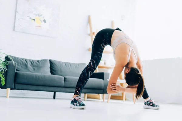 Selective focus of sportswoman bending while stretching at home — Stock Photo