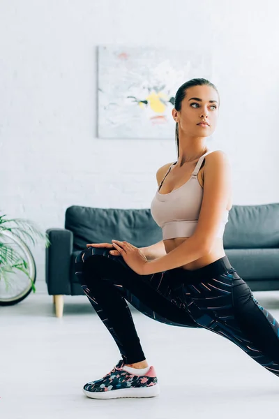 Young sportswoman looking away while doing lunges at home — Stock Photo