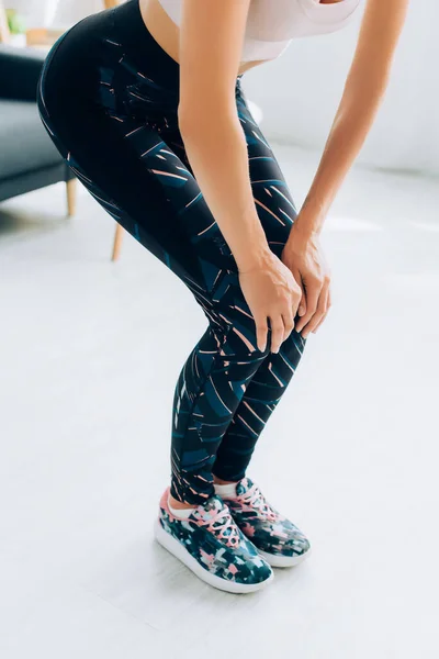 Cropped view of sportswoman warming up legs at home — Stock Photo