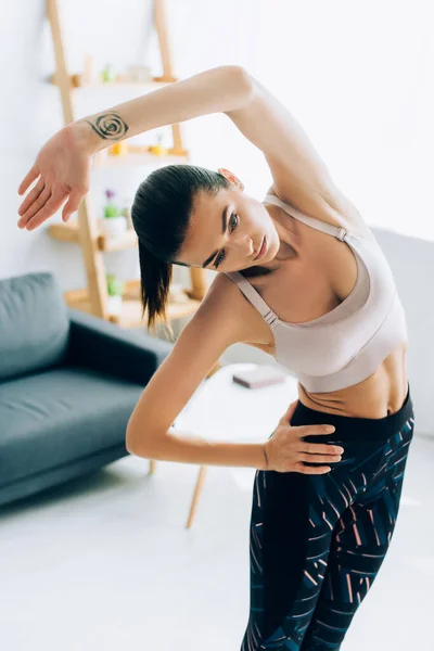 Desportista morena com a mão no quadril exercitando em casa — Fotografia de Stock