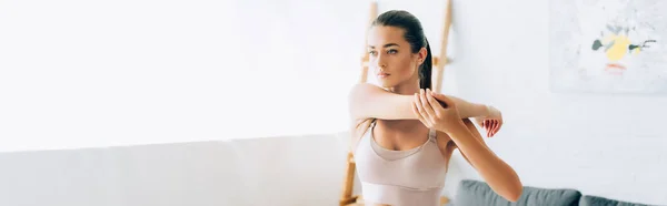 Panoramic orientation of brunette sportswoman stretching arms in living room — Stock Photo