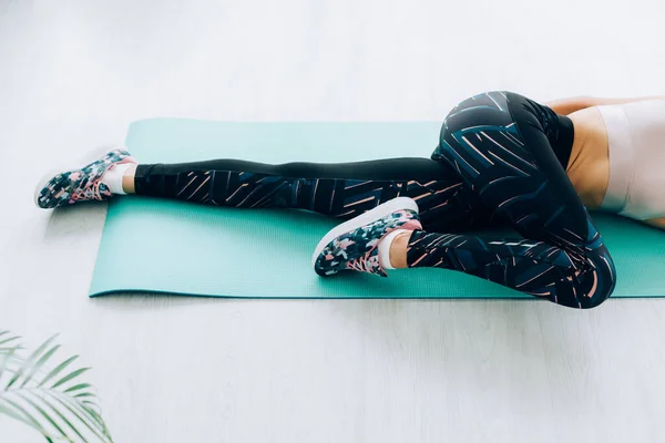 Cropped view of woman in sneakers and sportswear stretching on fitness mat at home — Stock Photo
