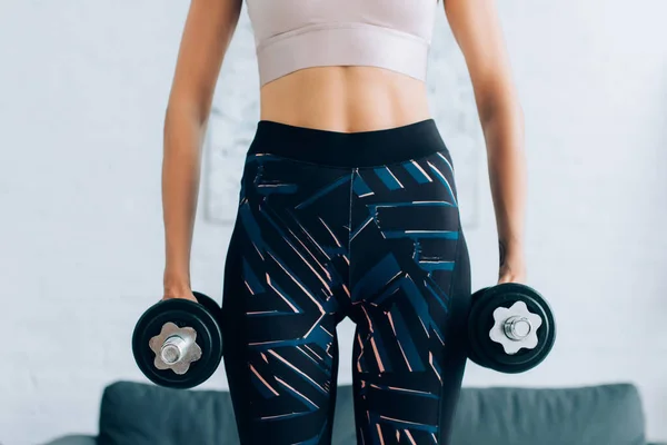 Cropped view of fit sportswoman holding dumbbells at home — Stock Photo
