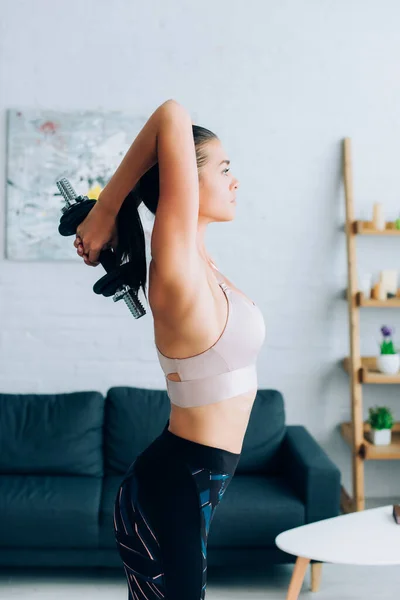 Vista lateral de la deportista en forma haciendo ejercicio con mancuerna en casa - foto de stock