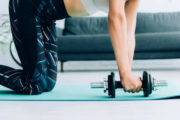 Vista ritagliata della sportiva che tiene i manubri sul tappeto fitness a casa — Foto stock