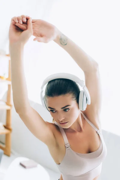 Selektiver Fokus der brünetten Sportlerin im Kopfhörer beim Training im Wohnzimmer — Stockfoto