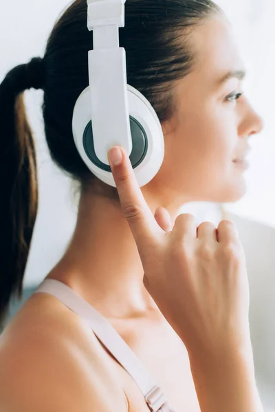 Concentration sélective de la jeune femme brune touchant les écouteurs tout en écoutant de la musique à la maison — Photo de stock