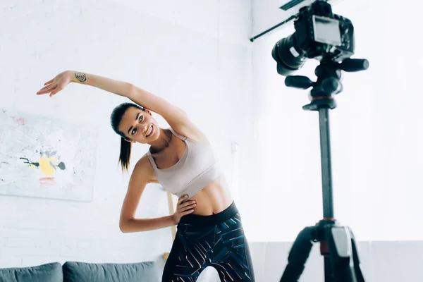 Enfoque selectivo de la deportista en forma haciendo ejercicio cerca de la cámara digital en casa — Stock Photo