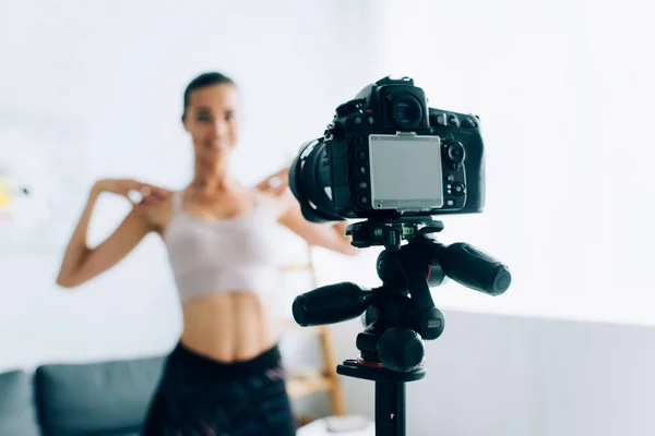 Selective focus of digital camera on tripod and sportswoman training at home — Stock Photo