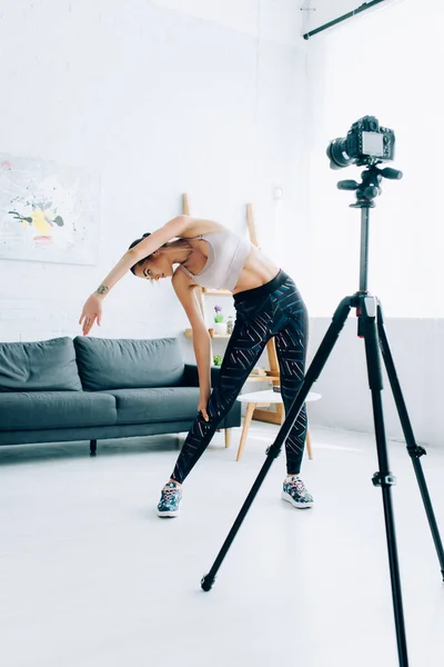 Selektiver Fokus der jungen Sportlerin, die sich in der Nähe der Digitalkamera im Wohnzimmer streckt — Stockfoto