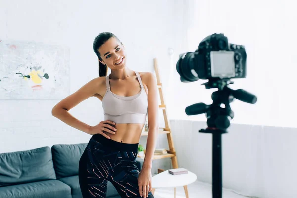 Selective focus of sportswoman with hand on hip looking at digital camera at home — Stock Photo