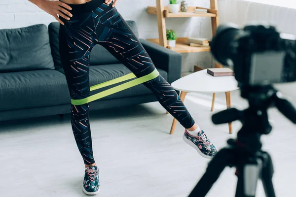 Cropped view of fit sportswoman training with resistance band near digital camera on tripod — Stock Photo