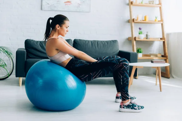 Side view of sportswoman working out on fitness ball in living room — Stock Photo