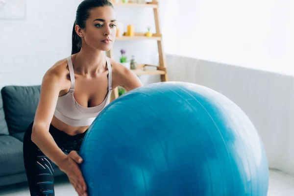 Selective focus of young sportswoman holding fitness ball while doing squat in living room — Stock Photo