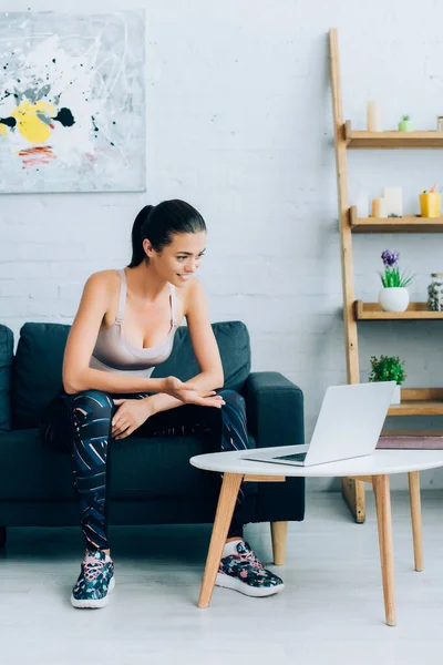 Sportswoman having video call on laptop while sitting on couch at home — Stock Photo