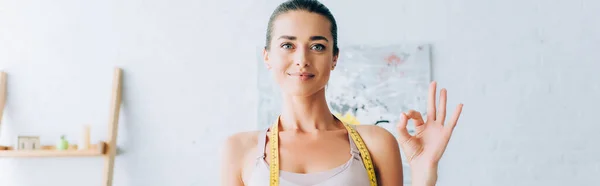 Panoramic shot of sportswoman with measuring tape around neck showing ok gesture at camera — Stock Photo