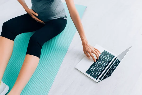 Cropped view of pregnant woman using laptop on fitness mat at home — Stock Photo