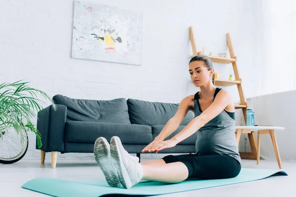 Concentration sélective de la jeune sportive enceinte étirant sur tapis de fitness à la maison — Photo de stock