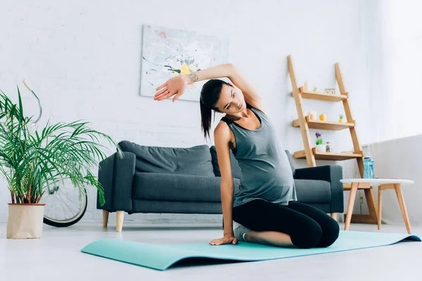 Selective focus of pregnant sportswoman warming up on fitness mat at home — Stock Photo