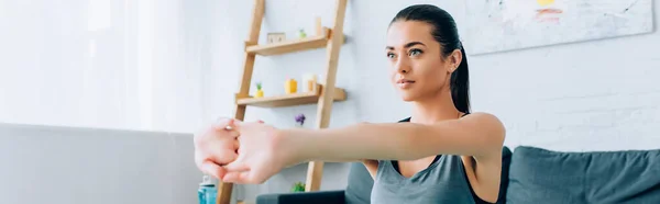Panoramic shot of brunette sportswoman stretching arms at home — Stock Photo