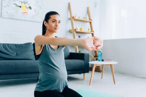 Pregnant woman stretching arms on fitness mat at home — Stock Photo