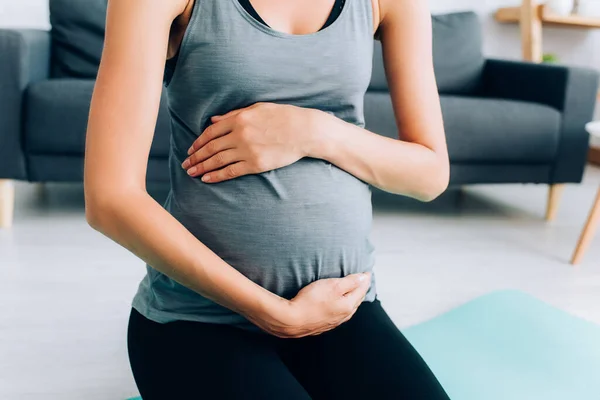 Vista cortada de esportista grávida tocando barriga no tapete de fitness — Fotografia de Stock