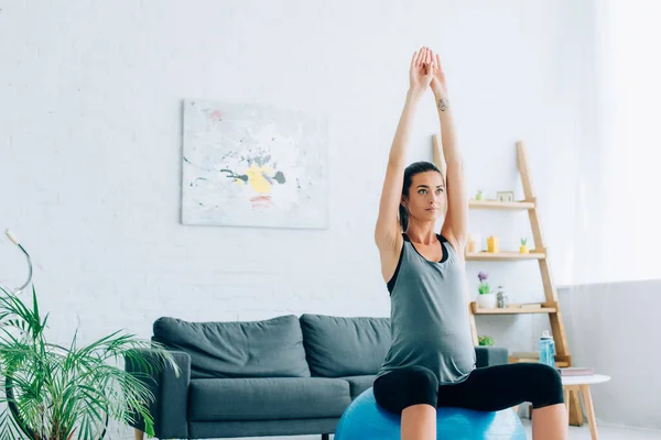 Young pregnant sportswoman training on fitness ball in living room — Stock Photo