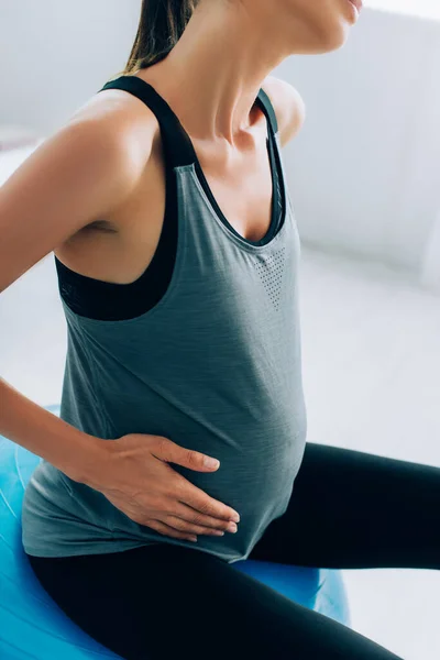Обрізаний вид вагітної жінки в спортивному одязі, що сидить на фітнес-кулі — стокове фото