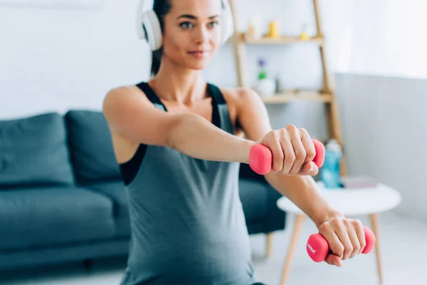 Enfoque selectivo de la mujer embarazada en el entrenamiento de auriculares con mancuernas rosadas en casa - foto de stock