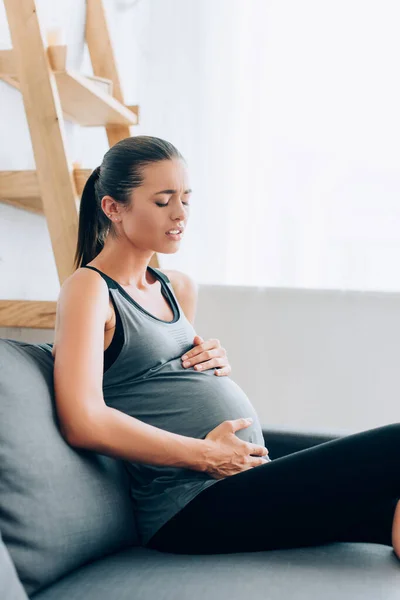 Concentration sélective de la jeune sportive enceinte souffrant de blessures sur le canapé à la maison — Photo de stock