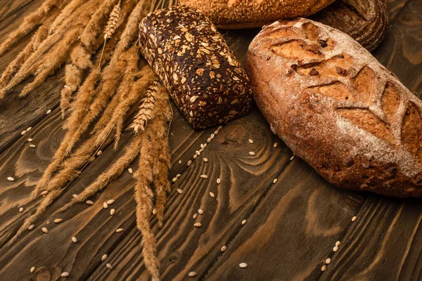 Pagnotte di pane appena sfornate con spighette su superficie di legno — Foto stock