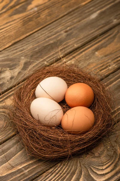 Fresh chicken eggs in nest on wooden surface — Stock Photo