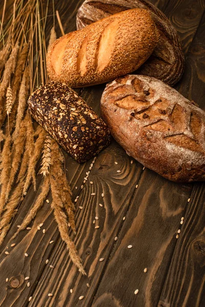 Pagnotte di pane appena sfornate con spighette su superficie di legno — Foto stock