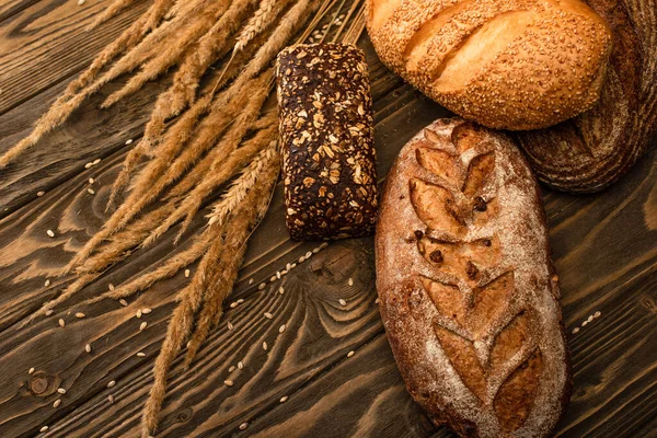 Pains de pain frais cuits au four avec des épillets sur la surface en bois — Photo de stock