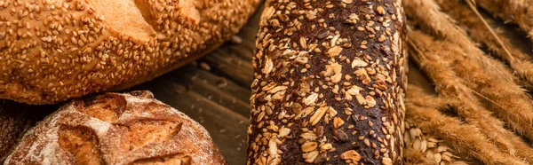 Vue rapprochée des pains frais cuits au four avec des épillets sur la surface en bois, vue panoramique — Photo de stock