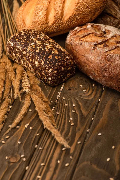 Fresh baked bread loaves with spikelets on wooden surface — Stock Photo