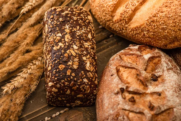 Pagnotte di pane appena sfornate con spighette su superficie di legno — Foto stock