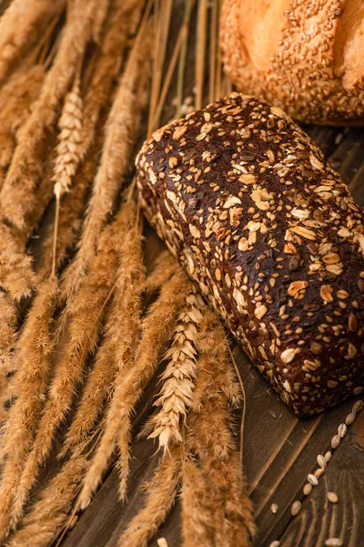 Close up view of fresh baked bread loaves with spikelets on wooden surface — Stock Photo