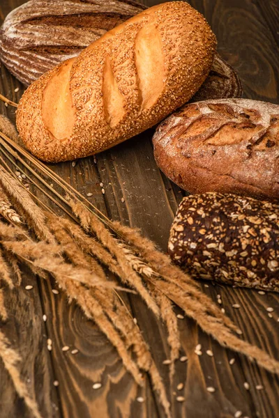 Fresh baked bread loaves with spikelets on wooden surface — Stock Photo