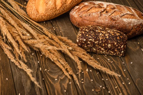 Pagnotte di pane appena sfornate con spighette su superficie di legno — Foto stock