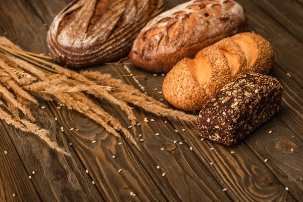 Fresh baked bread loaves with spikelets on wooden surface — Stock Photo