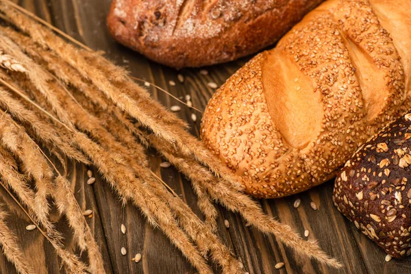 Pagnotte di pane appena sfornate con spighette su superficie di legno — Foto stock